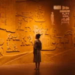 Back view of anonymous female traveler standing near ancient wall with Egyptian engraving