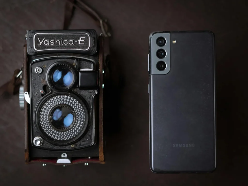 A vintage Yashica camera next to a modern smartphone, showcasing old and new technology.
