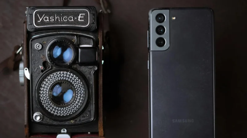A vintage Yashica camera next to a modern smartphone, showcasing old and new technology.