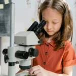 A curious girl examining a sample using a microscope in a classroom setting, focused on learning science.