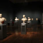 An art gallery with classical sculptures and framed art, showcasing elegant indoor lighting and design.