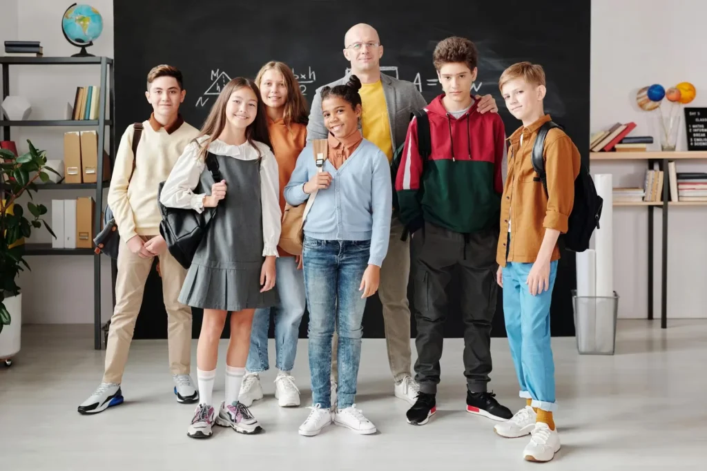Group of diverse teenagers posing with their teacher in a modern classroom.